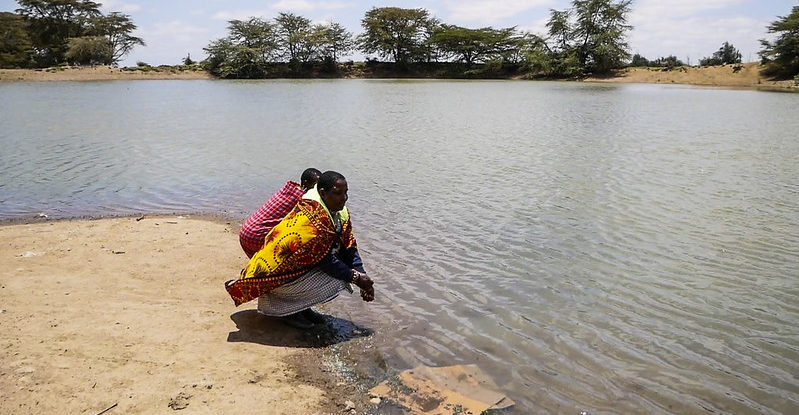 Two farmers crouch on the shoreline of a dam