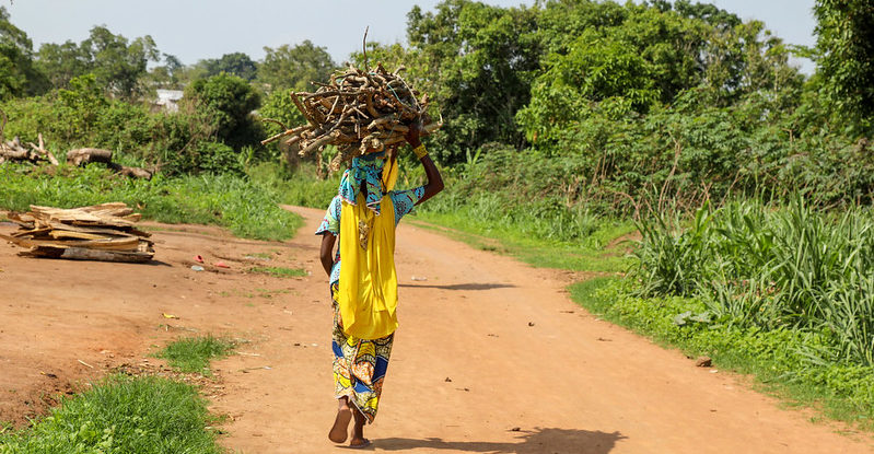 A woman walking along a dirt road with wood on her head